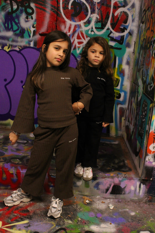 Kids wearing 'the minis.' ribbed brown and black long-sleeve outfits, street art background.