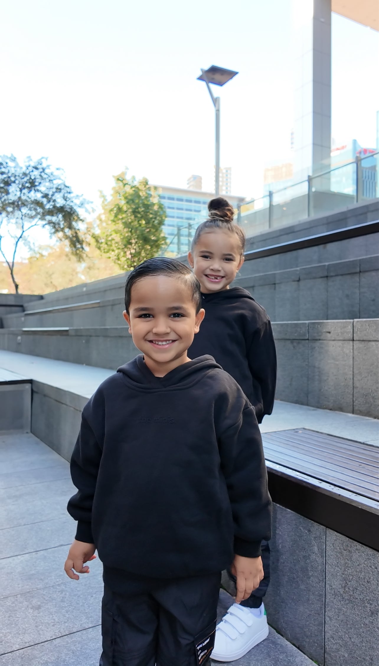 Smiling children in black hoodies. Boy in foreground wears black hooded sweatshirt with subtle front logo.