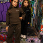 Two girls wearing 'the minis.' brown and black ribbed loungewear sets, featuring long-sleeve tops and matching pants.