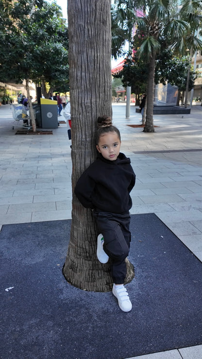 Young girl wearing a black hoodie, dark cargo pants, and white Velcro sneakers.