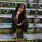 Young girl wearing a brown ribbed long-sleeve top & matching pants with grey athletic shoes, sitting on graffiti steps.