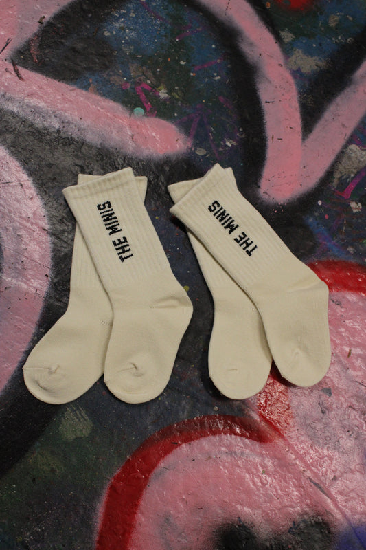 Off-white crew socks with black 'THE MINIS' logo text, displayed on a colorful graffiti background.